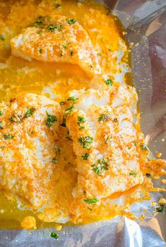 two pieces of fish covered in cheese and parsley on top of some tin foil