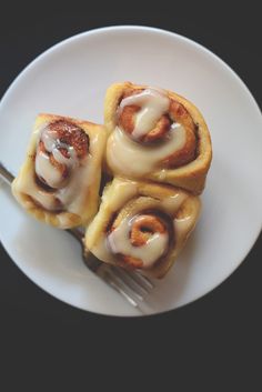 three cinnamon rolls on a white plate with a fork