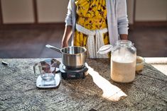 a woman standing next to a blender on top of a table with food in it