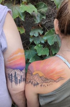 two people with tattoos on their arms looking at the mountains and trees in the distance