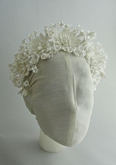 a white headpiece with flowers on it's top and bottom part, sitting on a mannequin