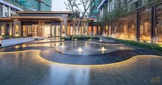 an empty courtyard with fountains and trees in the background at dusk, surrounded by tall buildings