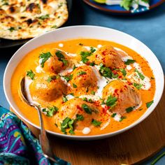 a bowl of soup with meatballs and sour cream on top, next to a plate of flatbreads