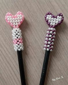 two pencils decorated with beads and bows on top of a wooden table next to each other