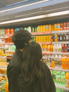 two people standing in front of a store filled with orange and green drinks, looking at each other