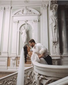 a bride and groom kissing on the balcony of a building with statues in the background