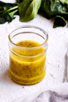 a glass jar filled with yellow liquid sitting on top of a white towel next to spinach leaves