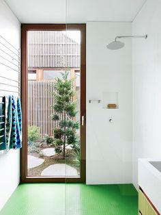 a bathroom with green flooring and a tree in the shower stall area, next to a large window