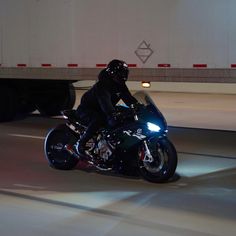 a man riding on the back of a black motorcycle down a street next to a semi truck