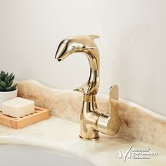 a golden faucet sitting on top of a bathroom sink next to a potted plant