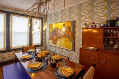 a dining room table with plates and place settings in front of a painting on the wall