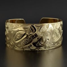 This cuff is hand-engraved and measures 1" wide by 6" long and was designed by First Nations artist Kelvin Thompson. This will fit a wrist between 6 1/4" and 6 1/2" in circumference. Custom lengths can be made on request. This piece is made to order and is titled 'Pod of Whales'.Whales usually signify longevity and strong community bonds due to their tendency to travel in close multi-family pods. In artworks, Orcas can be identified by a large, snub-nosed head; elongated nostrils; a wide, toothy Carved Symbolic Yellow Gold Jewelry, Yellow Gold Symbolic Carved Jewelry, Ceremonial Gold Bracelets With Polished Finish, Wide Band Yellow Gold Bracelets As Gift, Wide Band Yellow Gold Bracelets For Gift, Unique Yellow Gold Cuff Bracelet For Formal Occasions, Luxury Engraved Round Cuff Bracelet, Luxury Engraved Cuff Bracelet For Anniversary, Formal Engraved Bangle Cuff Bracelet