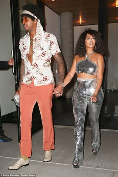 the man and woman are dressed up in disco outfits, one is holding his hand