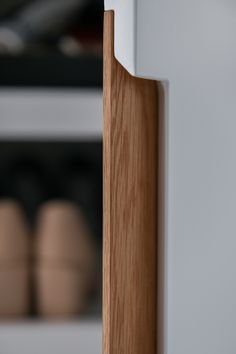 a close up of a wooden door handle on a white cabinet with shoes in the background