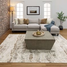 a living room with a couch, coffee table and rug on the floor in front of a brick wall