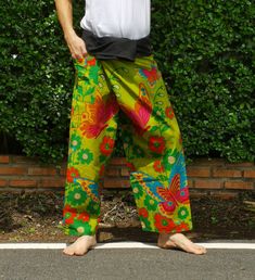 a man standing in front of a hedge wearing colorful pants