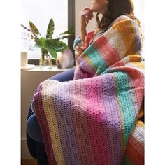 a woman sitting on a couch wrapped in a multicolored blanket and looking out the window