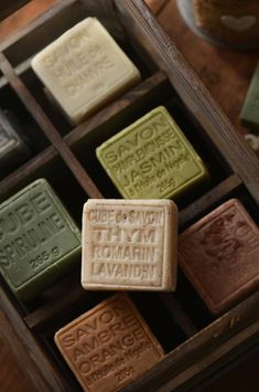 several soaps in a wooden box with writing on the front and bottom, all different colors