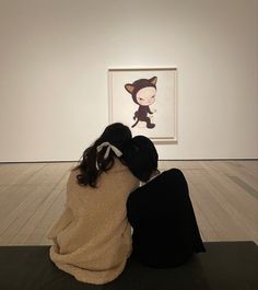 two people sitting on the ground in front of a painting