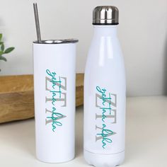 two white water bottles sitting next to each other on top of a table with a plant in the background