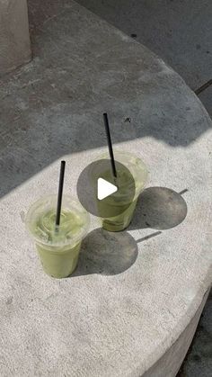 two plastic cups with black straws sitting on top of a cement slab next to each other