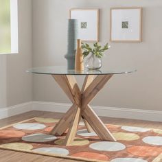 a round glass table with wooden legs in a living room next to a vase and two pictures on the wall