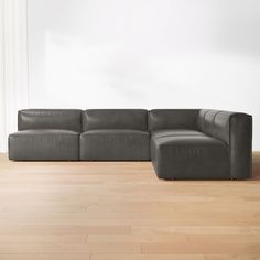 a gray leather couch sitting on top of a hard wood floor next to a white wall