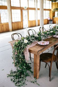 the table is set up with greenery and place settings for an elegant dinner party