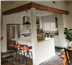 an open kitchen and dining room area with white cabinets, wood beams and counter tops