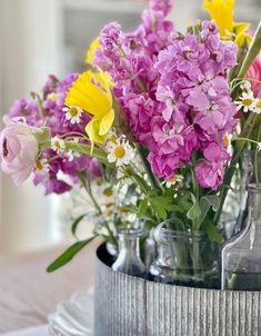 colorful flowers are in vases sitting on a tableclothed table cloth with an empty bottle next to them