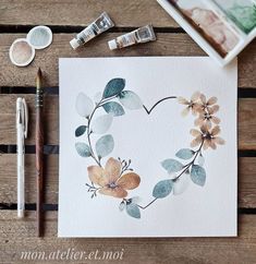 some watercolors are laying on top of a wooden table and there is a card with flowers in the shape of a heart