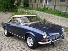 an old blue car parked in front of a brick building on a cobblestone street