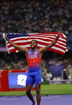 a man holding an american flag on top of a tennis court with his hands in the air