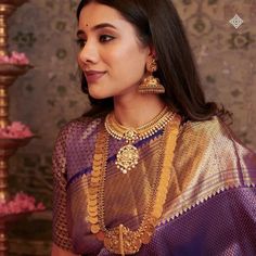 a woman in a purple and gold sari with jewelry on her neck, looking off to the side