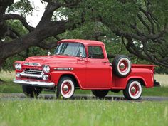 an old red truck parked on the side of a road in front of some trees