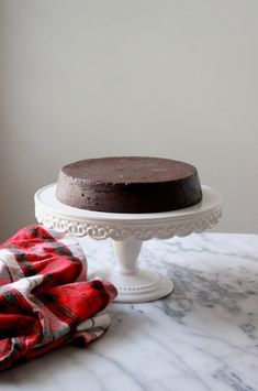 a chocolate cake sitting on top of a white cake stand next to a red and black checkered napkin