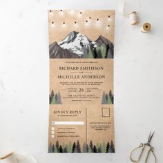 an image of a wedding card with mountains and pine trees on the front, surrounded by string lights