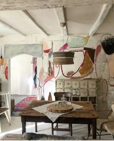 an old table and some chairs in a room with paintings on the wall behind it