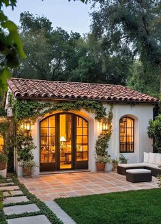 a small white house with lots of windows and plants on the outside, surrounded by greenery