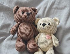 two crocheted teddy bears sitting next to each other on top of a bed