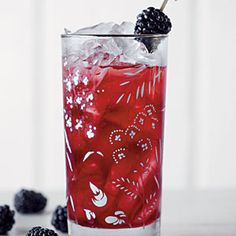 a glass filled with ice and blackberries on top of a white table next to berries