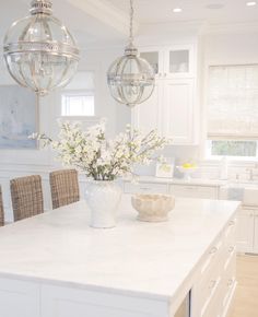 an image of a white kitchen with chandeliers on the ceiling and table in the middle