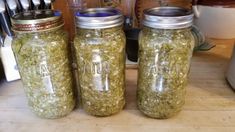 three jars filled with green stuff sitting on top of a wooden table next to knives