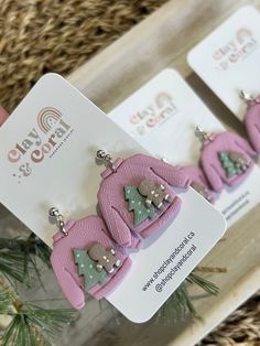 three pairs of pink elephant earrings with green and silver glitters on them, sitting in front of a christmas tree