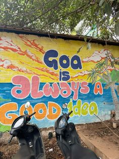 two motor scooters parked in front of a wall painted with the words god is always a good idea