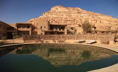 a large pool in front of a building with a rock face on the hill behind it