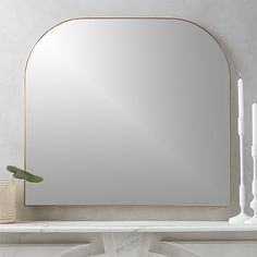 a mirror sitting on top of a white mantle next to candles and a potted plant