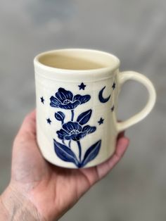 a hand holding a blue and white coffee cup with flowers on the outside, stars and moon designs