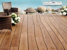 two wicker chairs sitting on top of a wooden deck next to the ocean with boats in the background