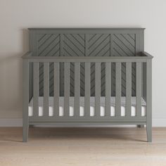 a gray crib in a white room with wood floors